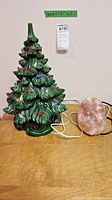 Ceramic green Christmas tree with colorful molded bulbs, 17 inches tall next to an electric pink salt lamp on a wooden surface, both with power cords.