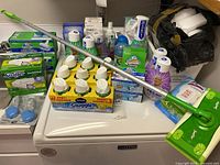 Full view of lot showing Swiffer Sweeper mop with handle, Snuggle air freshener multipack, Mr. Clean mists and wipes on a washing machine top.
