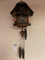 Full view of cuckoo clock showing clock face, figurines, and pinecone weights hanging below
