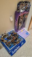 Photo of Glass Chess game box with detailed chess pieces arranged, visible Lego pirate/medieval themed figures and sealed Disney Wild Racers cars in blister pack, along with boxed Penny doll and princess fabric visible on floor