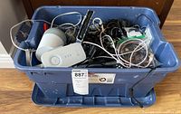 Blue storage tote filled with assorted electronic cables, corded and cordless phones, and chargers.