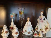 Photo showing Royal Doulton figurines, Royal Albert vase, champagne glass, and salt & pepper shakers on dark wood shelf