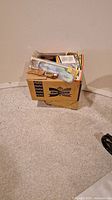 Cardboard box containing unopened fishing lures and miscellaneous items packed inside