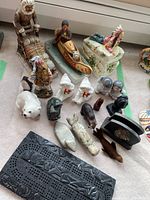Top view of Inuit-themed figurines and sculptures arranged on beige fabric. Includes ceramic and stone figures showing varied animals, native people, and symbolic Eskimo figures.