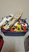 View of blue plastic storage tote filled with assorted Lego parts including the beige canoe-shaped Lego structure and a white Lego spaceship model