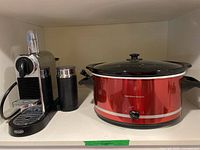 Photo showing DeLonghi Nespresso coffee maker with attached milk frother next to Hamilton Beach slow cooker on shelf.