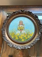 Front view of round framed painting showing girl holding bouquet in flower field