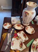 Overview of large vase, assorted trinket dishes, boxed cake server and linens on wood table