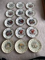 Full set of 15 plates arranged on carpeted floor showing various themed plates including Kate Greenaway Almanack and Christmas designs.