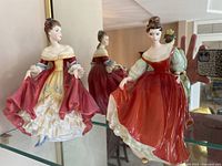 Two Royal Doulton porcelain figurines displayed side by side, one wearing white and red gown and other in red gown.