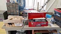 Red metal toolbox filled with tools on workbench along with boxes and other items