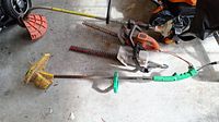 Lot of outdoor power tools including a Stihl gas-powered weed eater and various electric hedge trimmers and weeders laid on a garage floor.