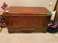 Front view of wooden heirloom chest showing chevron wood grain pattern, horizontal handle, and lock hole.