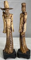 Front view of two Chinese carved bone figurines, male and female, standing on wooden bases.