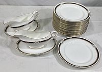Full view of the set showing stacked 18 salad plates, 2 gravy boats with saucers on a white surface