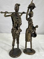 Photo showing two handcrafted cast metal African tribal sculptures of a man with a pole and a woman with pots.