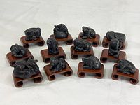 Set of 12 cast metal Chinese zodiac figurines shown on individual wooden stands with double arch base for scale and display.