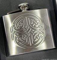 Close-up of stainless steel flask showing embossed Celtic knot design and hinged screw cap.