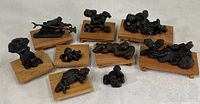 Nine dark cast metal miniature figurines on small rectangular wooden stands, arranged on flat surface.