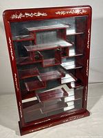 Front view of whole curio cabinet showing reddish-brown wood, intricate shelving and shell inlay designs along the frame