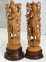 Front view of Krishna and Lakshmi sandalwood figurines standing on dark wood bases, showing detailed carvings