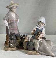 Two Lladro porcelain figurines, woman painting pot and man standing with pottery, detailed view on table.