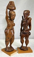 Full view of two wooden African sculptures, one woman with container on head and one man holding animal