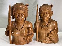Front view of both carved wooden indigenous hunter busts, showing full figures and detailed facial features