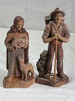 Front view of both wooden figurines depicting shepherd and shepherdess with lambs, showing size and condition