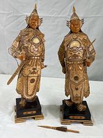 Two vintage Chinese warrior figurines standing side by side on a plain background, showing full height and details.