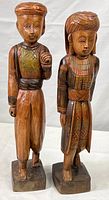 Front view of both wooden Thai figurines, male on left, female on right, showing their painted traditional clothing and standing poses.