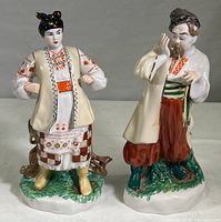 Two vintage Ukrainian porcelain folk figurines together, showing front and side views with detailed traditional costumes and colors.