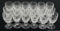 Eighteen short-stem sherry glasses arranged in rows on a black surface