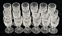 Full view of set of 18 Waterford Colleen crystal cordial aperitif glasses arranged in rows on a black surface.