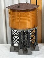 Front angled view of the Lionel water tower showing amber tank, brown roof, and black lattice base with feet.