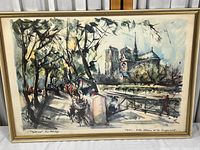 Full view of framed watercolor print showing a street scene with Notre Dame Cathedral in the background and bouquinistes along the pathway, housed in a gold trimmed frame.