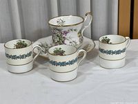 Photo showing three small Wedgwood cups and one floral patterned coaster or saucer, all bone china.
