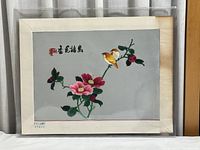 Full view of unframed traditional embroidery depicting birds and flowers with visible paper edges and discoloration