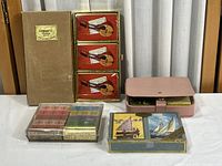 Five sets of vintage playing cards and pink leather case arranged on a table including Congress and ship-themed designs