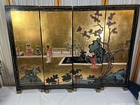 Front view of all four panels showing the gold reflective background with painted Asian figures, flowers, rocks, and landscapes in Chinoiserie style. Hinged panels stand upright.