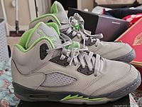 Side angle view of the pair of grey and neon green Air Jordan 5 Retro youth sneakers, showing mesh panel and sole.