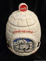 Front view of white ceramic igloo cookie jar with polar bear design, red 'Serve Ice Cold' text, and Coca-Cola logo cap on lid.