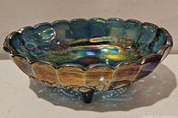 Angled side view of blue iridescent carnival glass bowl showing scalloped edge, floral pattern, and 4 toes.