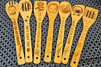 Top-down photo showing all eight wooden utensils with etched horror movie characters and quotes arranged horizontally on a patterned cloth surface.