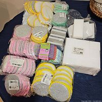 Large lot of assorted new cleaning sponges and pads arranged on a table showing different colors and types, all in plastic packaging.