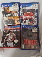 Four PS4 game cases: Battlefield Hardline, NHL 21, UFC 3 PlayStation Hits edition, Daymare. All cases show pre-owned pricing stickers.