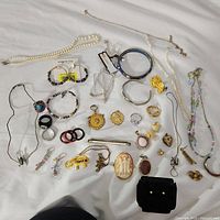 Lot of assorted vintage and modern jewelry laid out on a white surface including necklaces, rings, earrings, bracelets, and brooches.