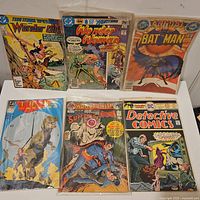 Photo showing six vintage comic books featuring Teen Titans, Wonder Woman (2 issues), Batman, Justice League of America, World's Finest Superman Batman, and Detective Comics.