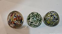 Three vintage glass paperweights arranged side by side showing different colors and patterns
