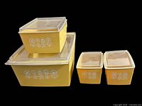 Set of four yellow mid-century style plastic storage containers with clear lids, featuring white floral patterns, shown together on black background.
